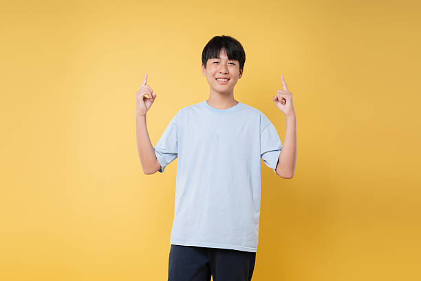 istock Cheerful young person pointing upwards with both hands standing against a bright yellow backdrop 2236217811