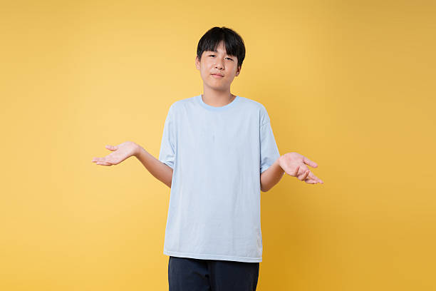 istock Boy with hands out shrugging Represents confusion doubt or uncertainty on a vibrant yellow background 2236217813