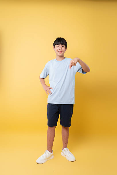 istock Smiling young man pointing downwards against a bright yellow backdrop embodying youthful charm 2236218366