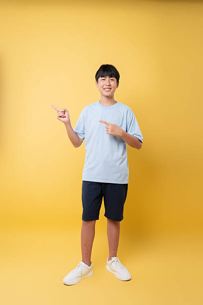istock Smiling young person points off camera dressed casually against vibrant yellow backdrop Friendly pose 2236218371