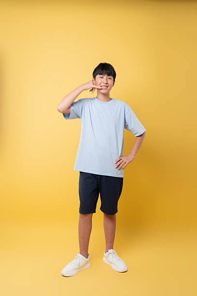 istock Smiling boy on yellow backdrop making a call gesture wearing casual clothes and sneakers 2236218384