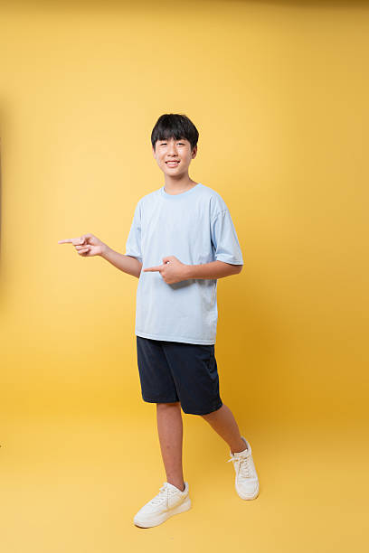 istock Smiling teen points in studio with a bright solid yellow backdrop Casual and inviting pose 2236218388