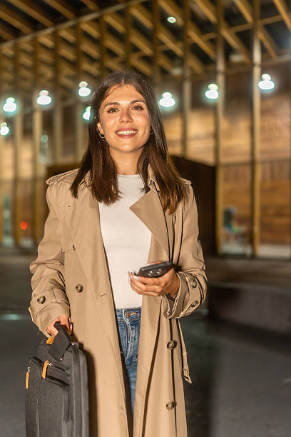 istock Woman smiling holding briefcase and mobile phone at night 2236219117