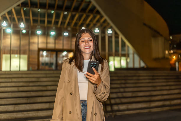 istock Young woman smiling while checking smartphone at night 2236219122