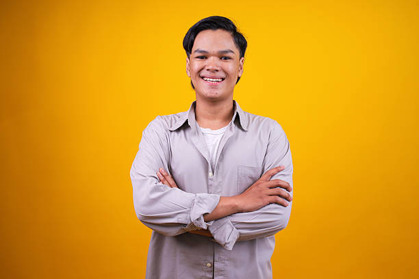 istock Young Asian Man Smiling Confidently While Crossing Arms Isolated on Yellow Background 2236220273