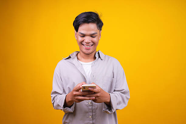 istock Asian Young Man Using Cell Phone Isolated on Yellow Background 2236220817