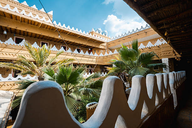 Courtyard featuring palm trees and cultural statues surrounded by traditional architecture. The design includes intricate patterns and natural elements, creating a harmonious environment in a classic Arabian style.