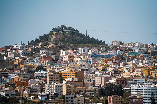 Expansive cityscape featuring a densely packed urban environment with colorful buildings and a prominent green hill in the background, highlighting Abha's unique architectural blend and natural landscape.