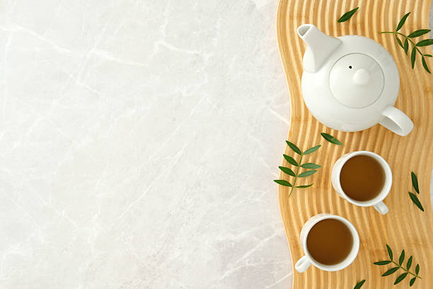 istock Serene tea scene with white teapot and cups on wavy wooden tray over marble surface, decorated with green leaves for a natural and minimalist style. 2236227607