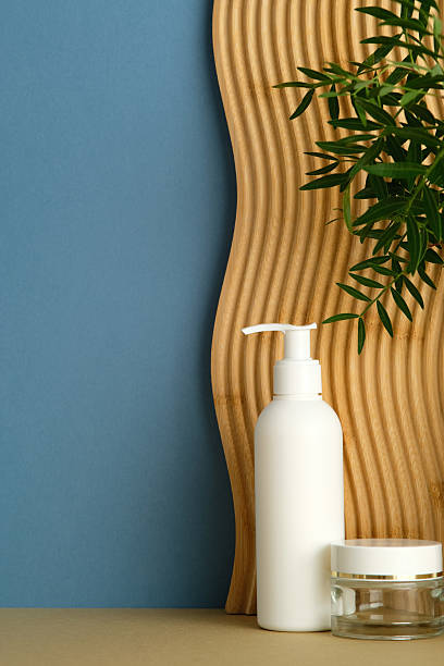 istock White pump bottle and clear jar with white lid, green foliage, wavy panel, blue background, minimalist skincare scene. 2236227975