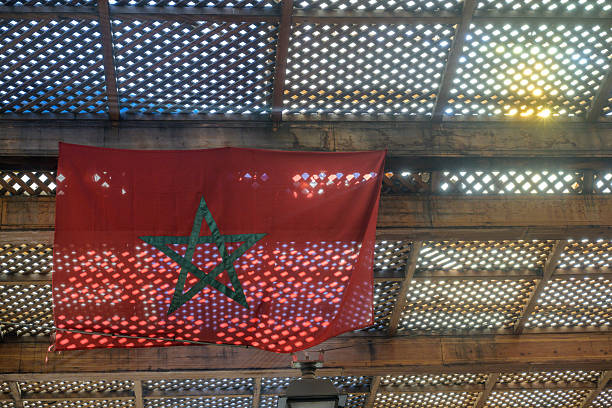 Sunlight filters through the lattice roof, illuminating the Moroccan flag in Fez. The vibrant colors contrast with the bustling souk below.