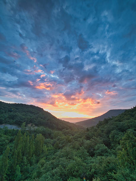 Dramatic Sunset Over a Lush Valley - A breathtaking and colorful sunset with vibrant clouds over a forested valley, conveying peace and natural beauty.