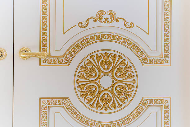 The gold and white door has a floral design on it. The door is made of wood and has a gold trim