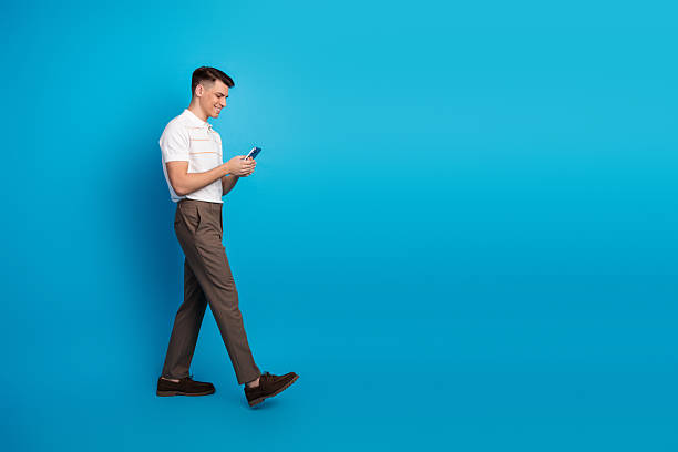 istock Stylish young man using smartphone while walking against vibrant blue background expressing cheerful and casual lifestyle 2236239662
