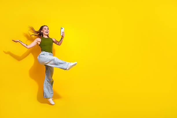 istock Excited young woman holding smartphone posing joyfully on bright yellow background capturing a fun moment 2236240431