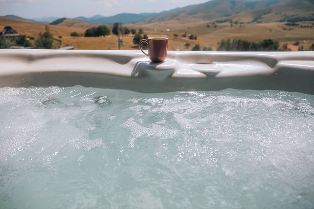 Coffee cup on the edge of an outdoor hot tub, with panoramic mountain view in the background. Concept of wellness, leisure, and travel.