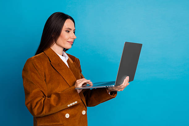 istock Confident businesswoman holding a laptop while working in a modern office setting with blue backdrop 2236241429