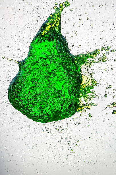 A vibrant splash of green liquid frozen mid-air, forming an abstract shape with scattered droplets suspended around it against a white background, captured in sharp high-speed detail.