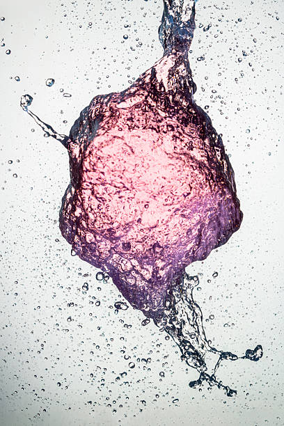A splash of pink liquid frozen mid-air, forming a textured abstract shape with droplets scattering around, suspended against a white background in sharp high-speed detail.