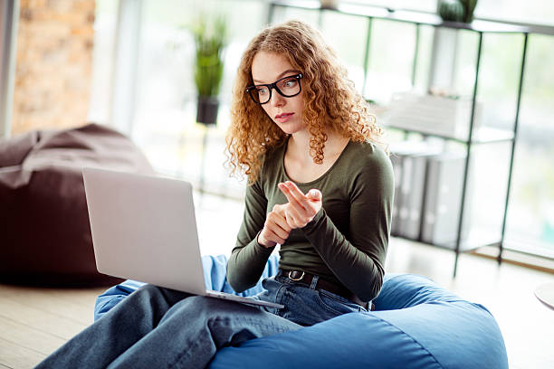 istock Young woman using a laptop while sitting on a beanbag in a cozy interior workspace with a focused expression 2236245401