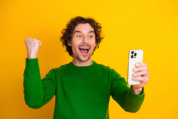istock Excited young man celebrating achievement while using smartphone against vibrant yellow background 2236250618