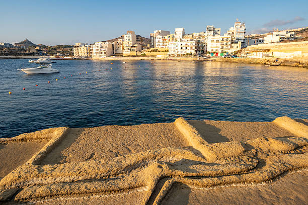 Qbajjar Bay, located on Gozo’s north coast between Xwejni Bay and Marsalforn, is a shallow inlet known for its historic salt pans carved into the rocks, some of which are still used today. The bay’s name comes from the Maltese word for “large salt pans.” It has a small sandy beach, rocky shoreline, and is popular for swimming, snorkeling, and fishing. Nearby, remnants of a coastal watchtower built by the Knights of St. John in the 18th century overlook the area, adding historic charm to this natural and cultural landmark.