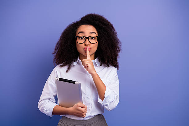 istock Professional woman in glasses gesturing silence while holding a tablet against a chic purple background 2236251132