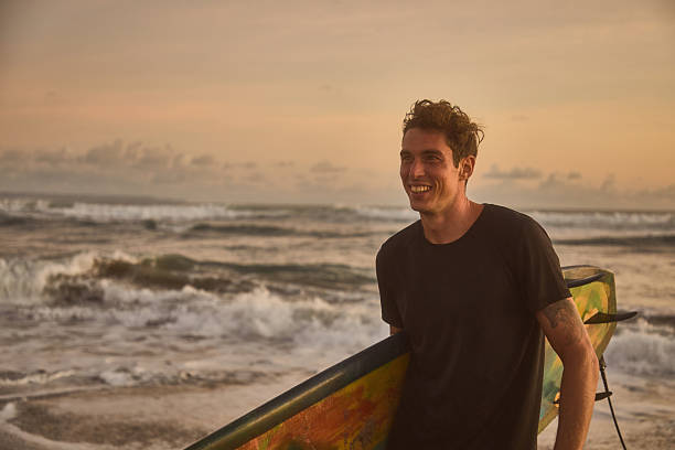 istock Smiling surfer with board at sunset by the ocean shore 2236251833