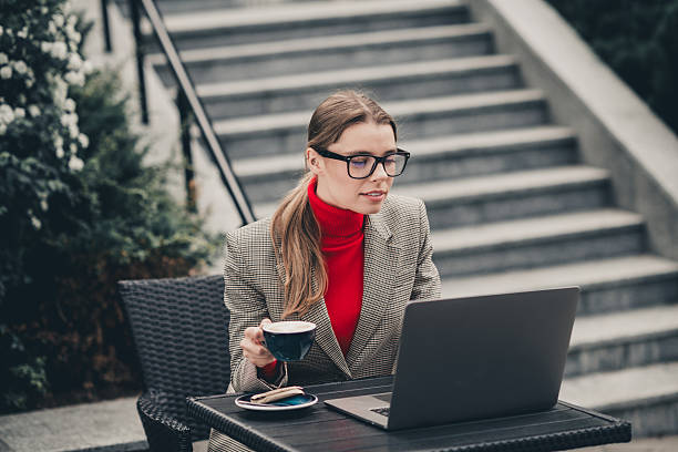 istock Confident businesswoman working on laptop outdoors with coffee while dressed stylishly in a vibrant city setting 2236253115