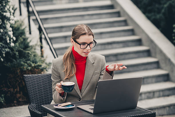 istock Young businesswoman in formal attire using a laptop outdoors, enjoying a coffee break while engaging in work discussions 2236253116