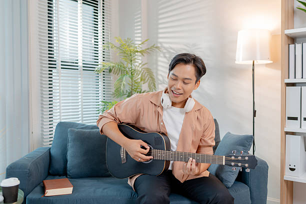 istock A young man is joyfully playing guitar in his living room, enjoying the rhythm while practicing chords. His relaxed posture and smile reflect happiness and musical passion. 2236254583