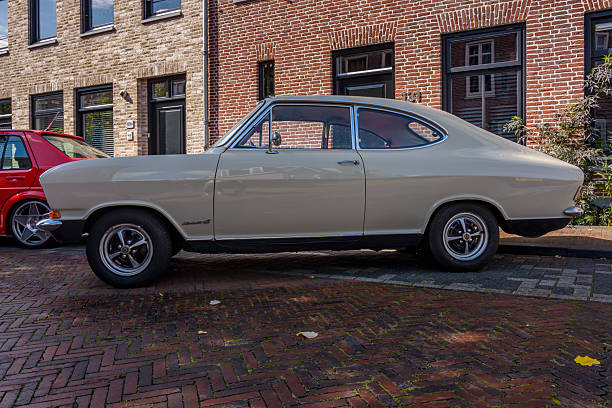 A vintage green car, possibly parked on a brick surface, with an open hood revealing mechanical parts It has a chrome grille and round headlights The scene suggests daytime and lacks people or move