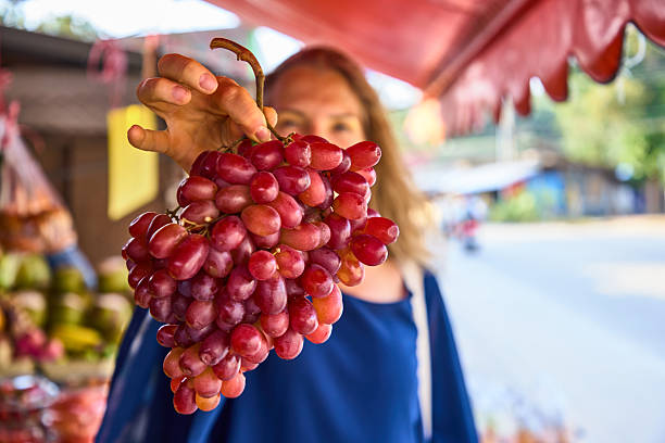 Woman holding fresh red grapes at a market with a blurred street background