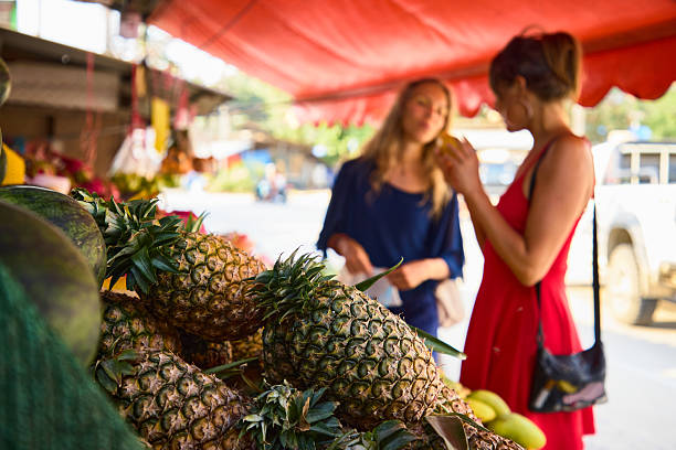 Women shopping for fresh pineapples at a vibrant outdoor fruit stand