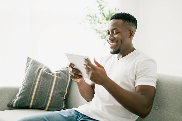 istock Black men wearing white shirt on sofa holding tablet 2236258921