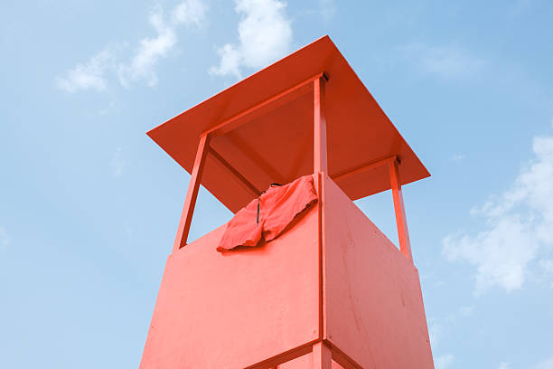 Red lifeguard hut standing tall on a summer day, featuring minimalist architecture with a pair of swim shorts hanging, conveying themes of summer, safety, and vacation