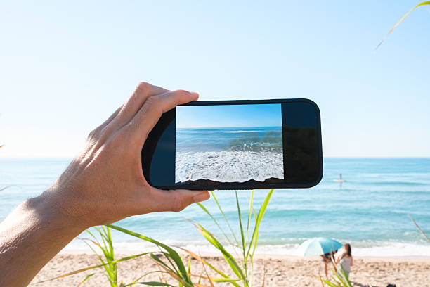 istock Hand holding phone recording ocean waves on sunny beach 2236263501