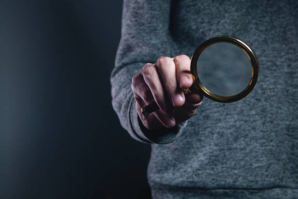 istock Man's hand holding a magnifying glass on a dark background. 2236273471
