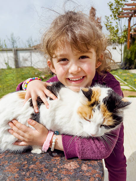 Child embracing a small cat while standing in a rural outdoor setting.