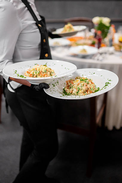 istock Waiter serving plated rice and vegetable dishes at a formal event. Professional service, elegant table setting, and catering atmosphere captured in motion 2236277592