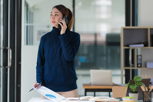 istock Image of an Asian businesswoman holding a document report and using a cellphone while working in an office. 2236279736