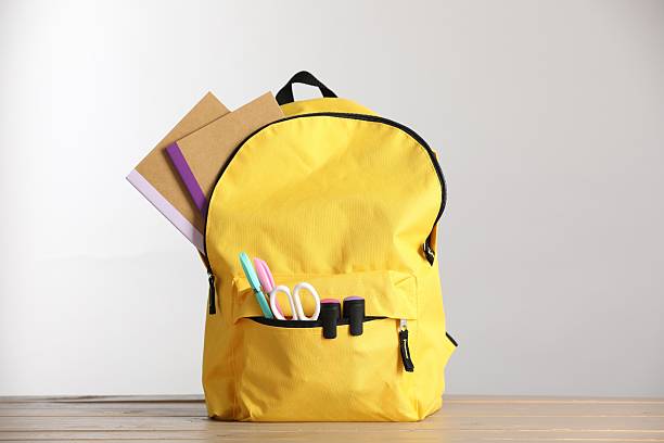 istock Yellow backpack with different stationery on wooden table against light background 2236279968