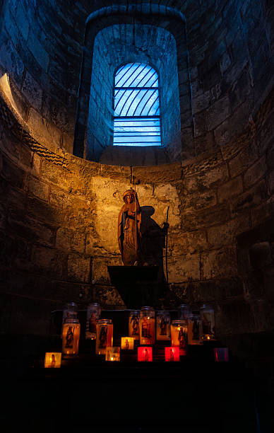 istock Statue of a saint with lit votive candles inside a stone chapel with a window. 2236290129