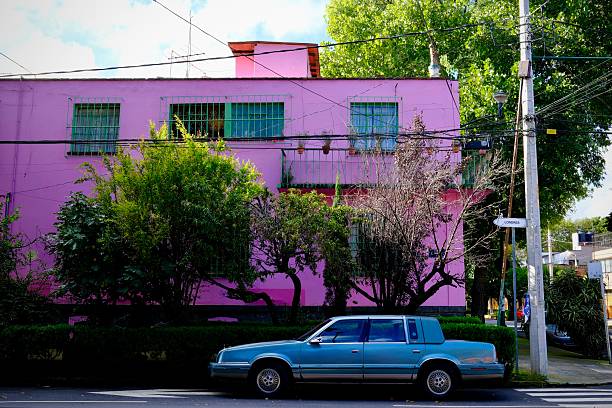 Mexico City, CDMX, Mexico – September 11, 2025: A bright pink apartment building with a blue car parked in front along a quiet Mexico City street.
