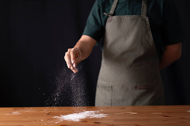 istock Chef hand sprinkling flour on a wooden table, preparing for baking 2236295050