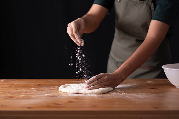 istock Baker preparing dough, sprinkling flour on rustic wooden table, baking at home 2236295264
