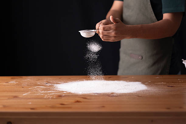 istock Person sifting flour on a wooden kitchen counter, preparing dough for baking 2236295272