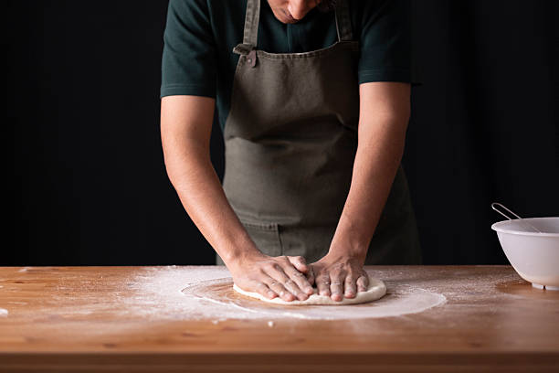Baker kneading dough on wooden table, preparing homemade bread or pizza