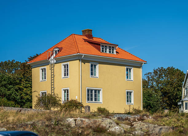 Yellow house with red tiled roof under blue sky.