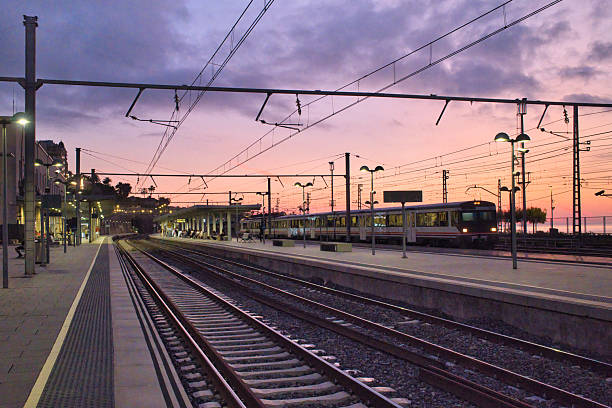 Early morning sunrise at Tarragona train station in Spain, where people wait on the platform as a train arrives. The image highlights urban commuting, transportation infrastructure, and the daily rhythm of mass transit in a city environment.